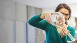 Female student uses large, round volumetric flask to complete an experiment. 