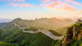 Sunset view of the Great Wall of China winding over surrounding mountains.