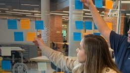 Students place sticky notes on a wall during an exercise in health innovation and entrepreneurship