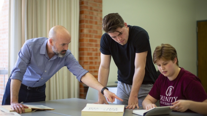 chad spigel pointing at a book next to two students