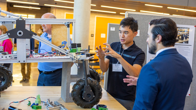 A student explains his engineering project to someone at the Summer Undergraduate Rsearch and Internship Symposium