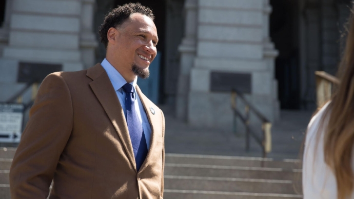Terris Tiller stands outside smiling in a brown suit