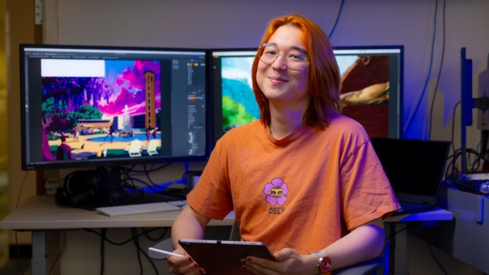 A student with orange hair and clothes sits in front of a computer.