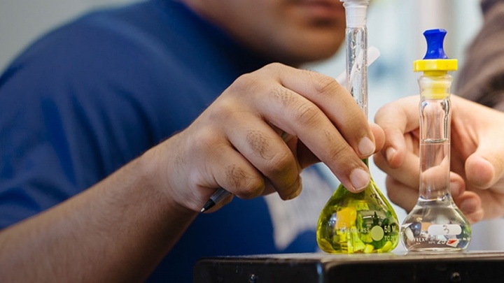 two hands hold two flasks with different colored liquids