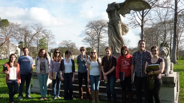 Students gather outside for a group photo in front of a winged statue