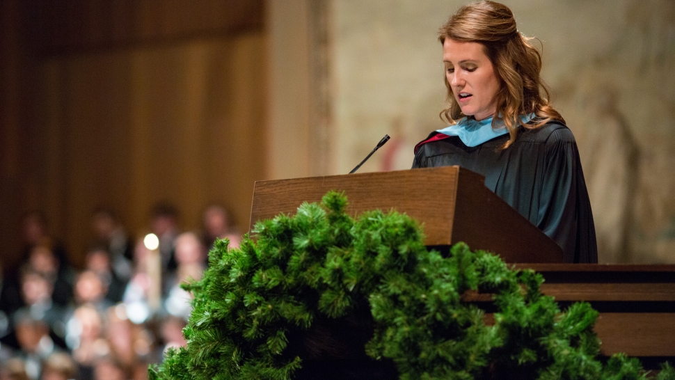 Jamie Thompson speaks at a podium wearing regalia