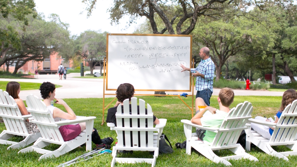 Math professor and students around a whiteboard outside