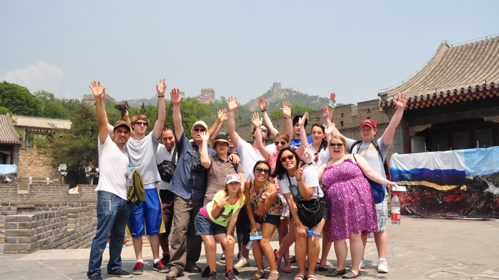 A group of students and faculty pose with their hands in the air in front of the Great Wall of China