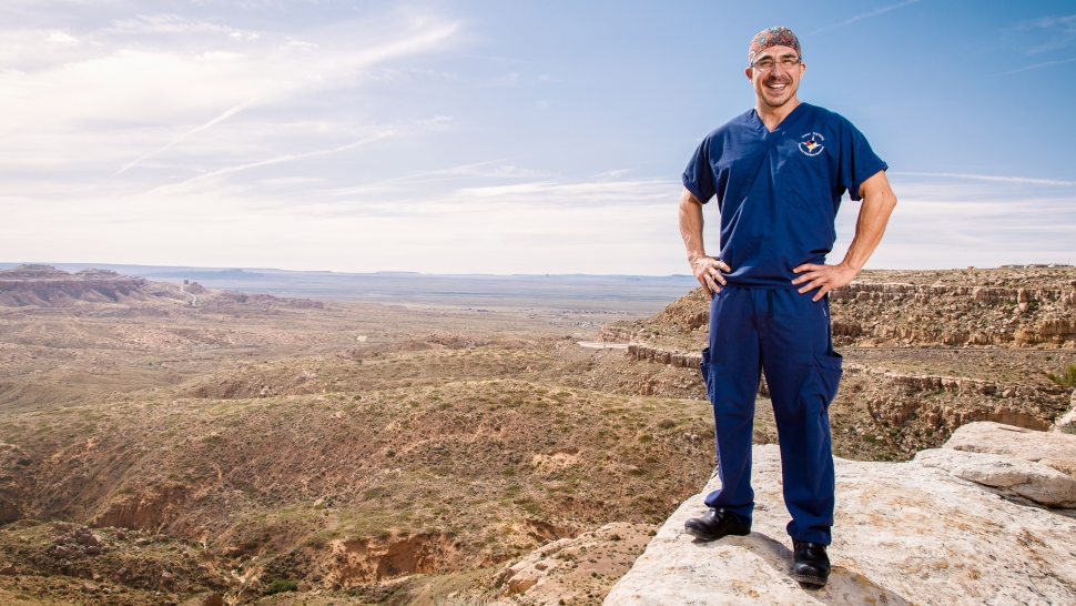 Keith Goss stands on a cliff with vast Native American landscape in the background