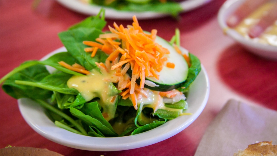 spinach salad with sliced cucumbers, shredded carrots, and honey mustard dressing in a white bowl on a red table