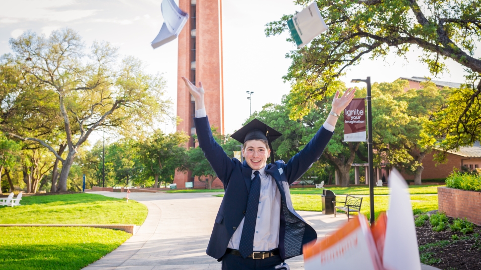 photo of recent graduate outside tossing books in the air and smiling