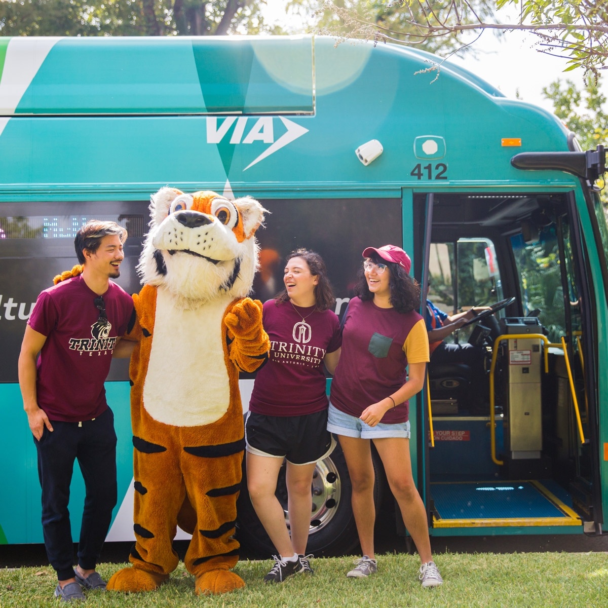 three students and the LeeRoy mascot stand in front of the VIVA culture bus