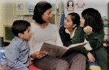 Three children listening to an adult reading an open book on her lap