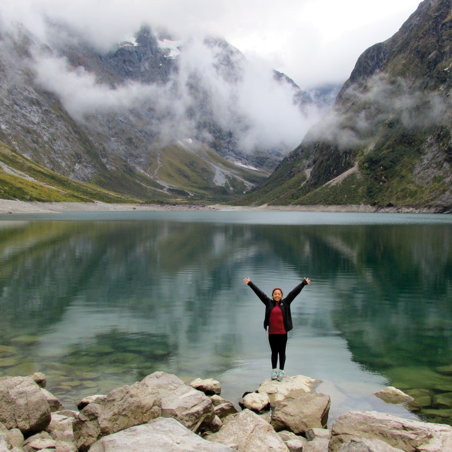 a student poses with arms outstretched at Lake Marian New Zealand