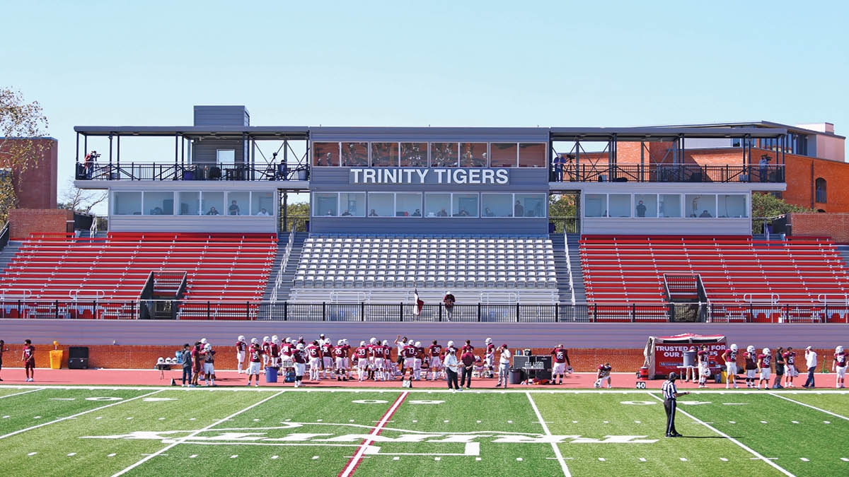 renovated home side of multi-purpose stadium, with new bleachers, press box, and suites. football players stand in front of it during a game.