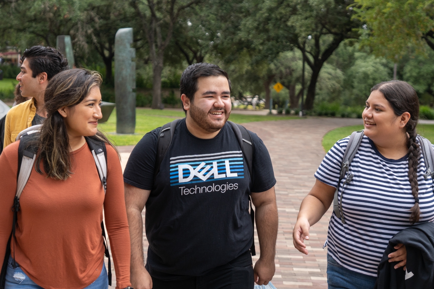 thomas pena wears a dell technologies shirt and walks near the magic stones on trinity's campus with friends