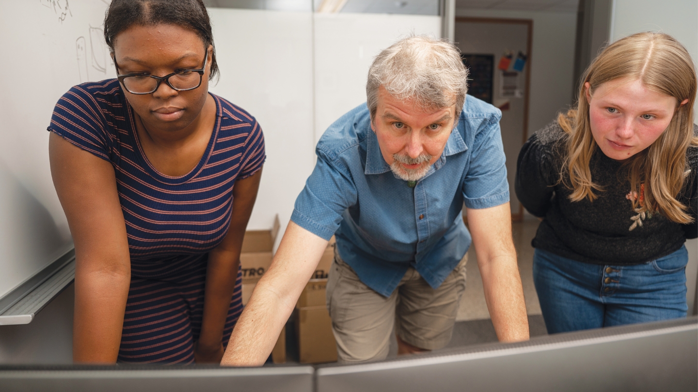 Hrbek (center) looks at a dual monitor while two students look on