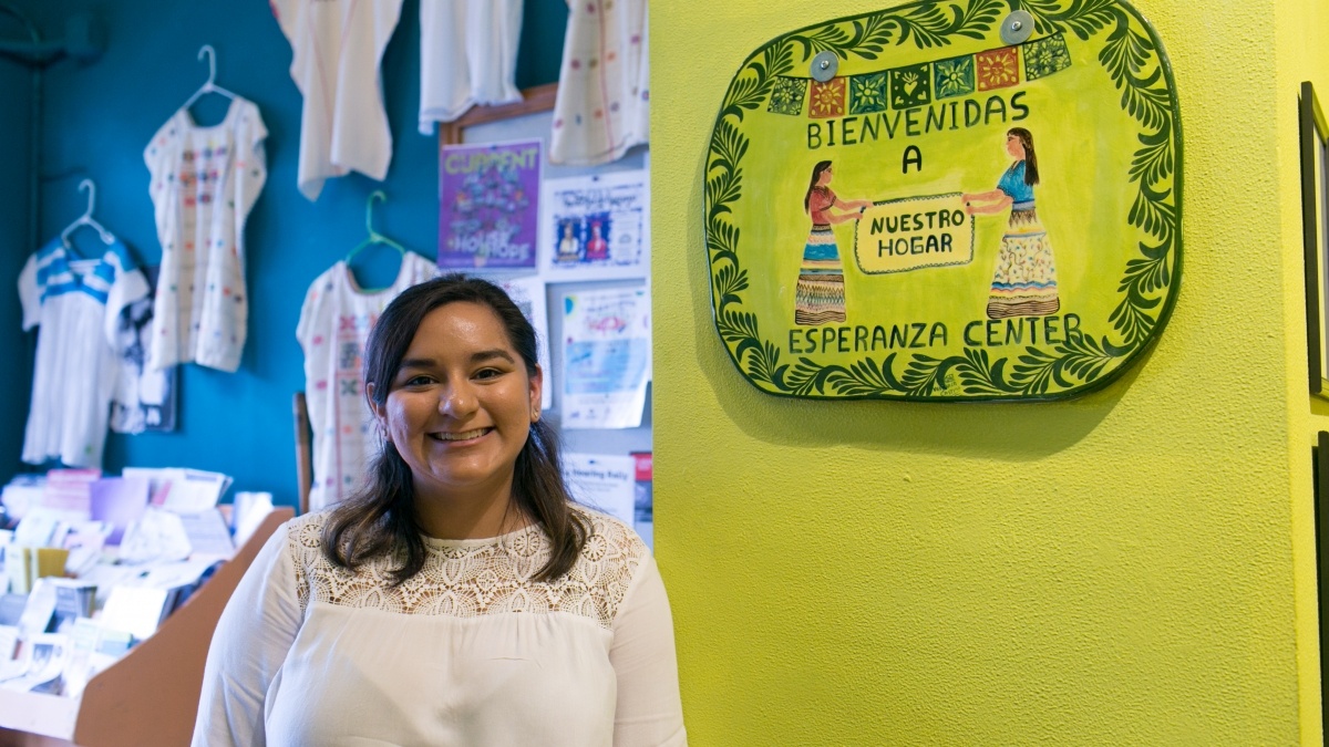 Student smiles in front of a sign at Esperanza Center that reads "bienvenidas" 