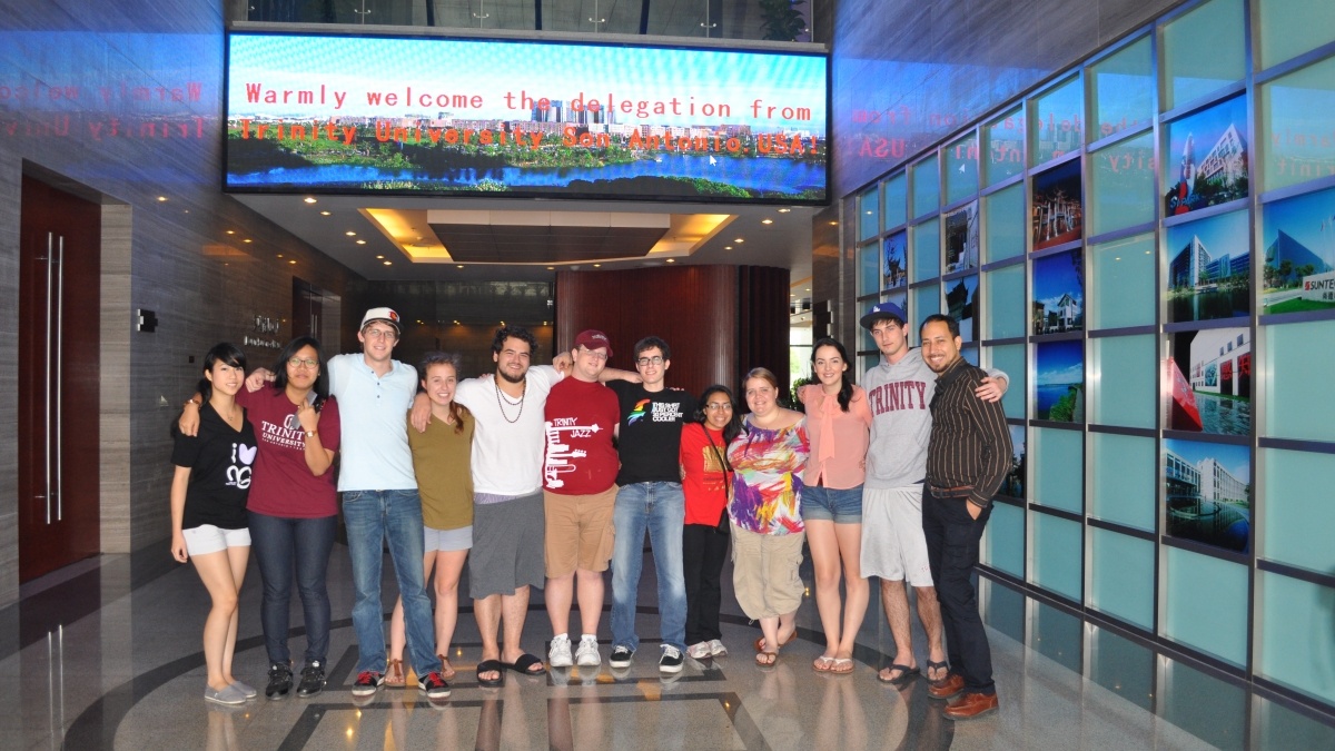 Group of faculty and students posing under sing that says "welcome delegation fro Trinity University"