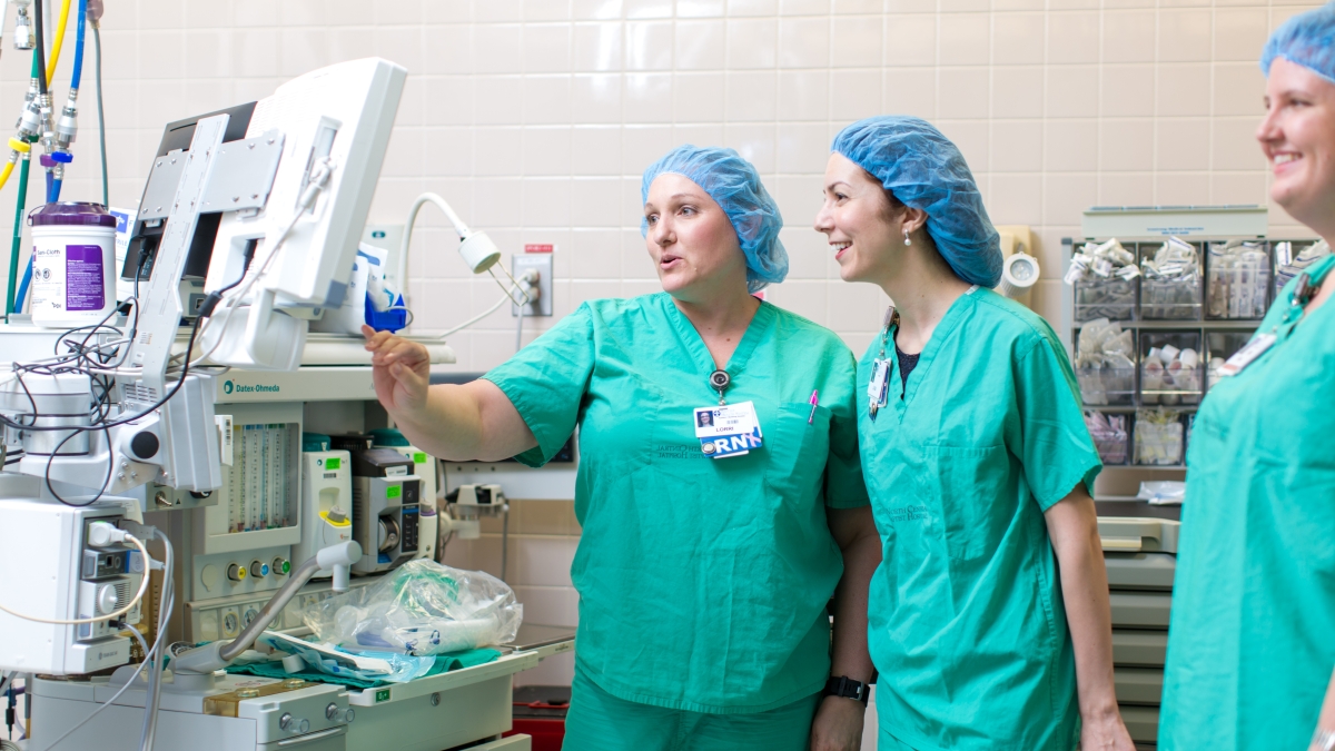 Three nurses observe a monitor in an operating room
