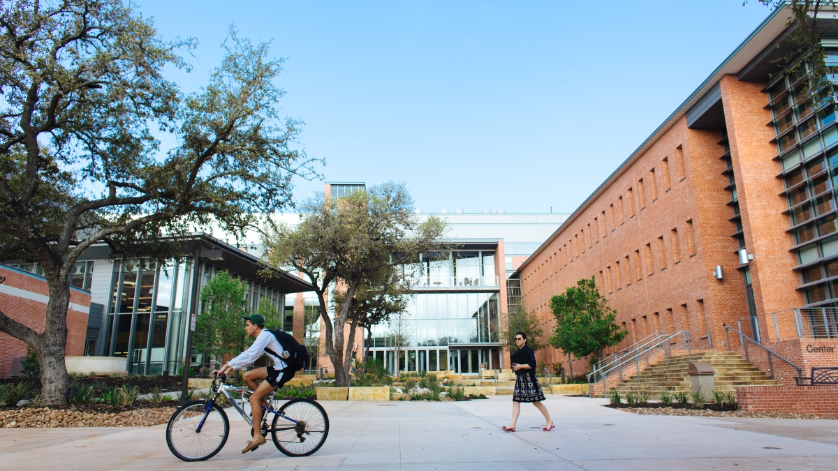 a student on a bicycle rides by the entrance to CSI