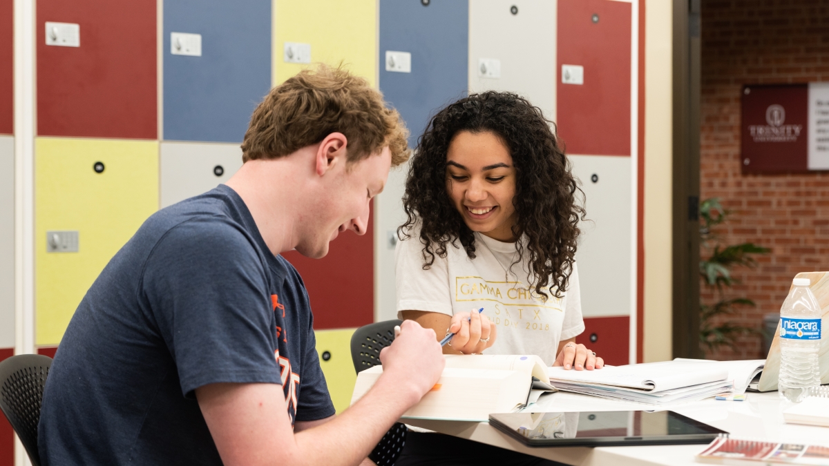 Two students in a tutoring sessions with several open books on a table